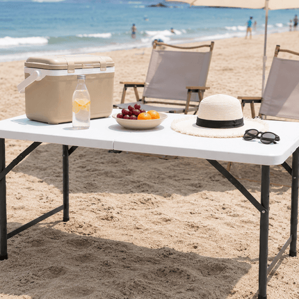 Portable folding camping picnic table on beach with outdoor chairs and picnic accessories